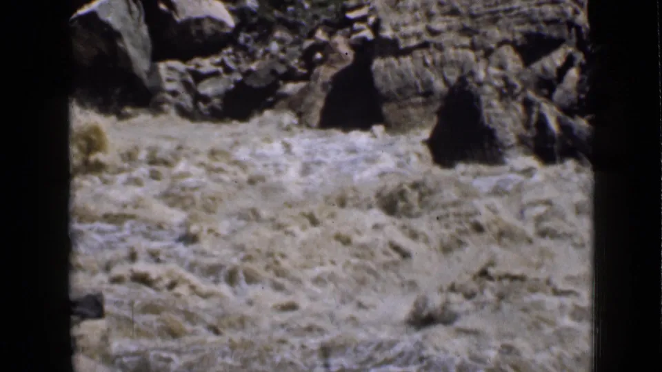 1939 Utah 8mm frame with muddy water surging below dark canyon rocks and scattered dry vegetation.