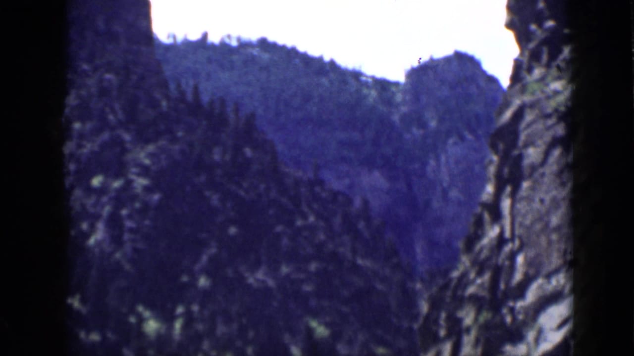 1939 Utah 8mm frame looking through a narrow canyon area toward dark rock walls and evergreen-covered slopes.