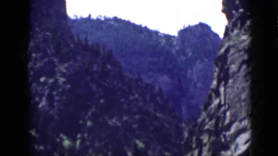 1939 Utah 8mm frame looking through a narrow canyon area toward dark rock walls and evergreen-covered slopes.