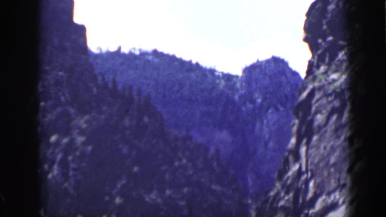 1939 Utah 8mm frame with a dark vertical rock face at the edge of a forested canyon slope.