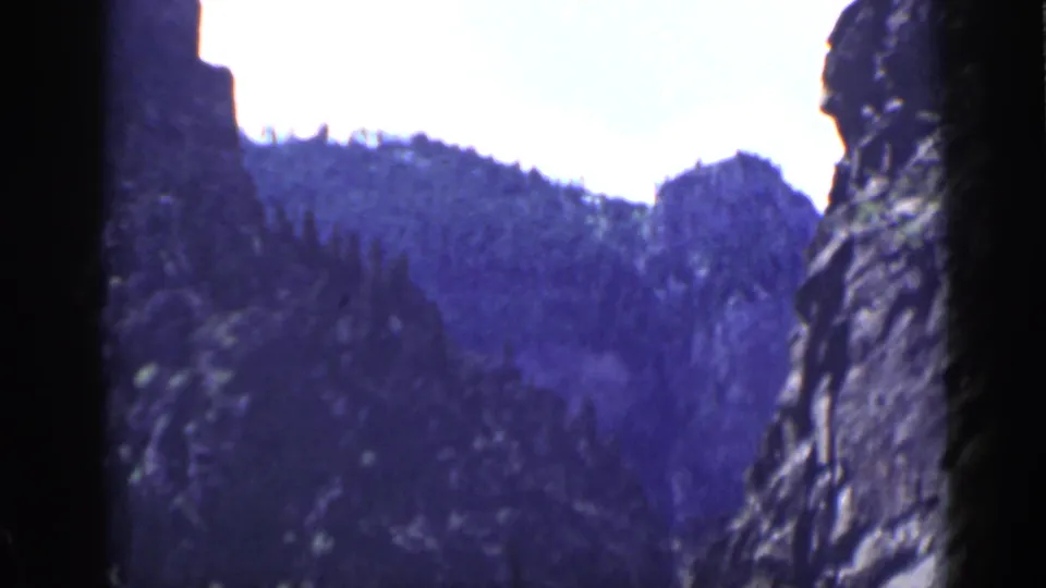 1939 Utah 8mm frame with a dark vertical rock face at the edge of a forested canyon slope.