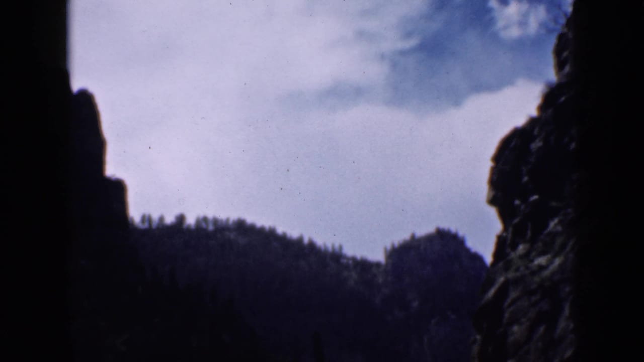 1939 Utah 8mm frame looking from a dark rocky canyon toward a distant forested ridge and cloudy sky.