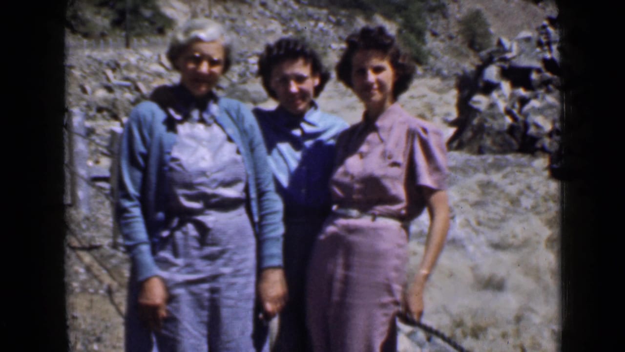 Three women pose together on a rocky hillside in daylight.