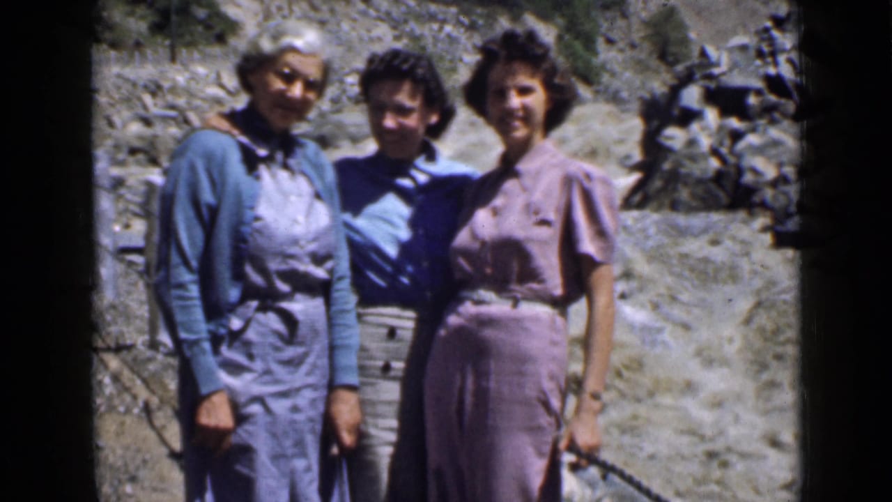 Three women pose closely on a rocky Utah overlook, with period clothing and a rope or rail visible beside them.