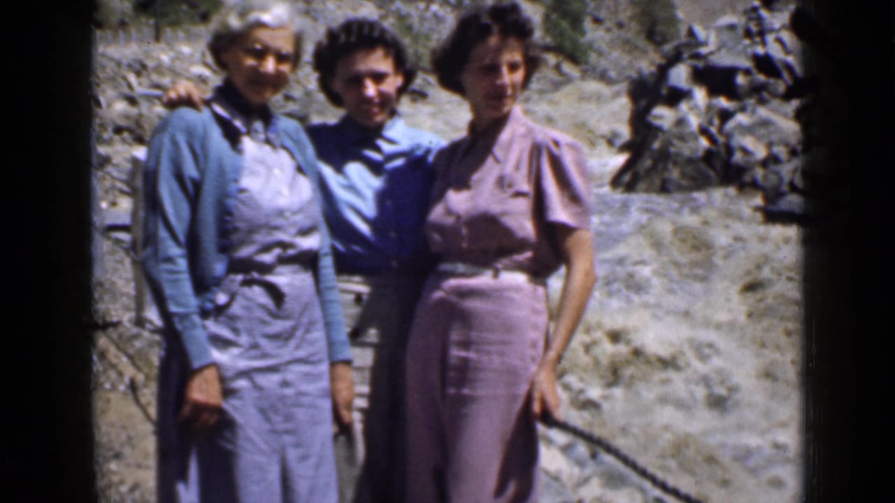 Three women stand close together on an outdoor trail beside a rocky slope.