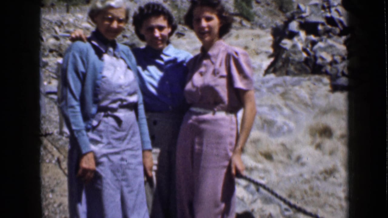 Closer home-movie frame of three women in period clothing posing on a rocky trail in Utah.