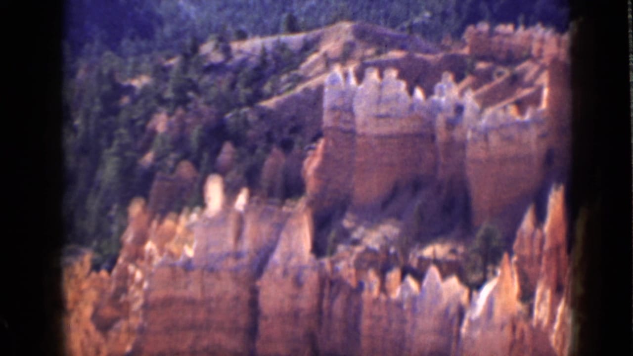 Orange hoodoos and pale rock caps below a dark forested hillside.
