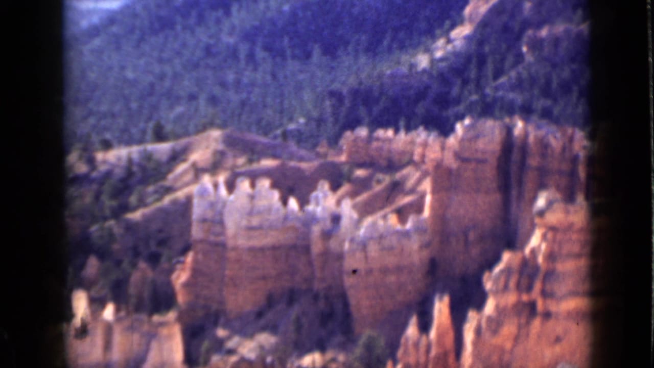 1939 Utah 8mm view of layered orange hoodoos and pale stone tops set against dense green mountain forest.
