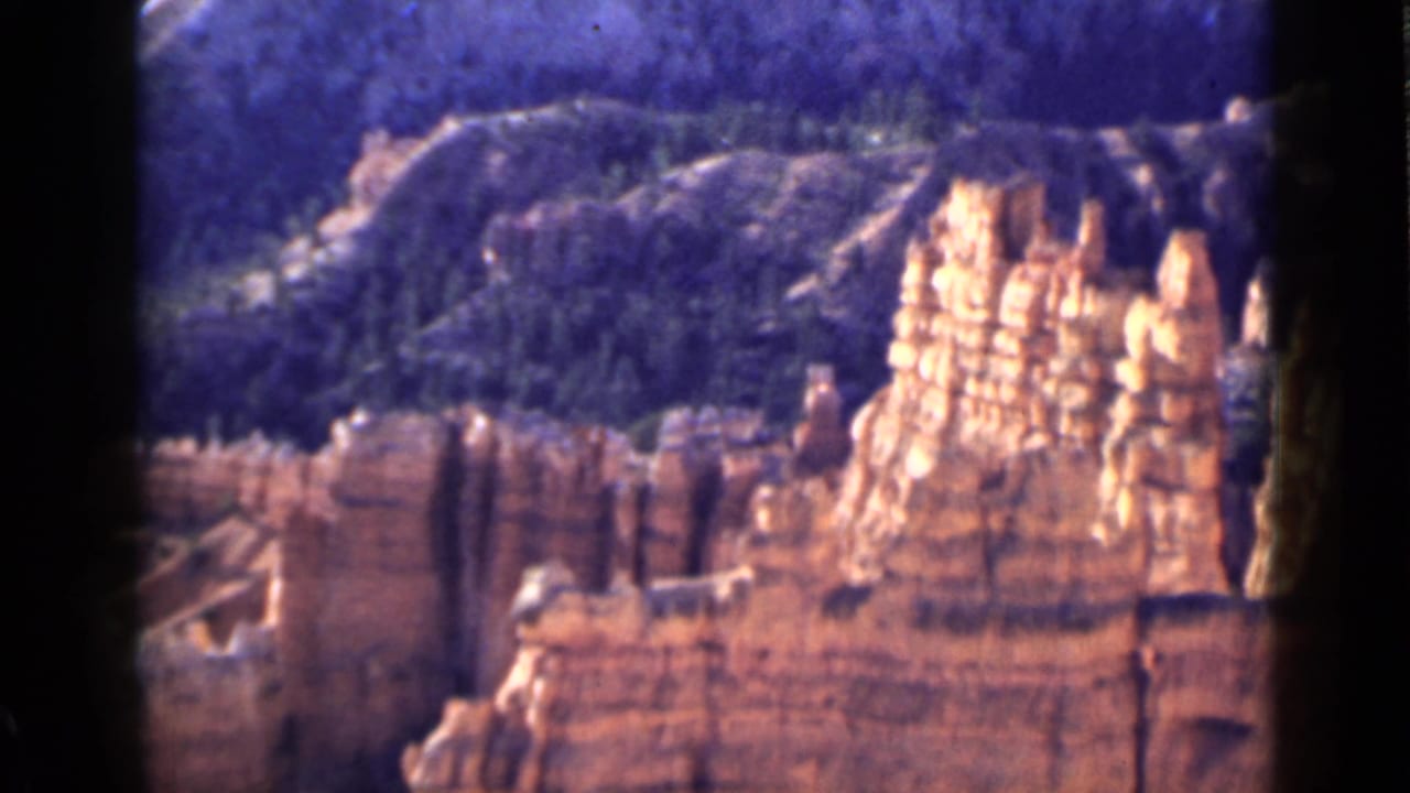 1939 Utah 8mm frame showing bright orange sandstone spires beside darker ledges with forested hills behind.
