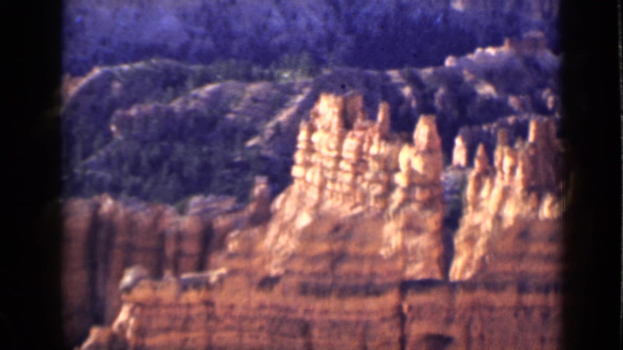 1939 Utah 8mm frame showing sunlit red rock spires and layered cliffs with dark wooded terrain behind them.