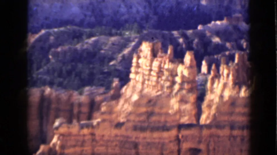 1939 Utah 8mm frame showing sunlit red rock spires and layered cliffs with dark wooded terrain behind them.
