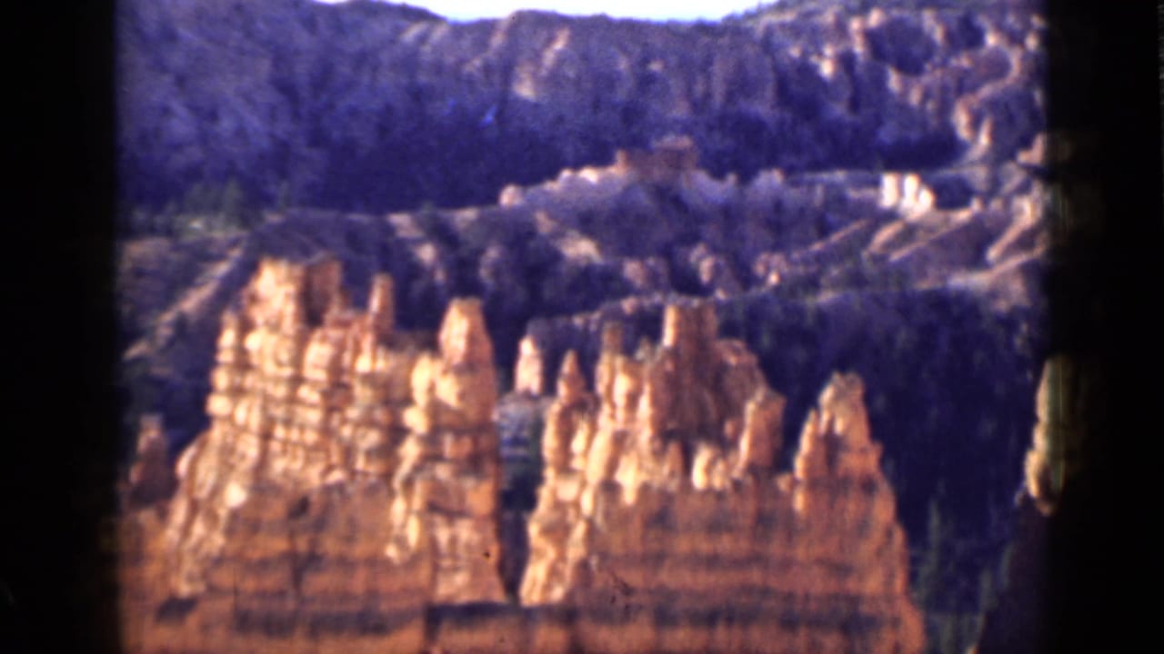 Layered canyon wall with red rock spires and wooded ridgeline.