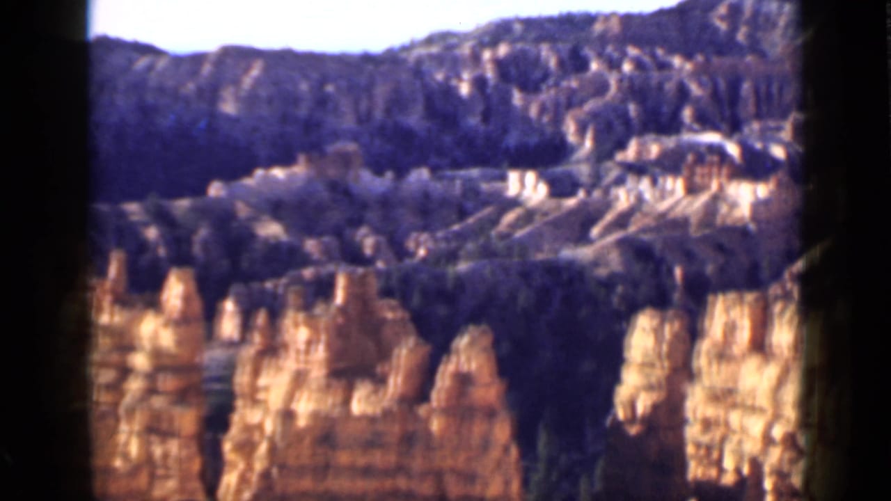 1939 Utah 8mm view looking across red rock formations, pale eroded slopes, and dense green vegetation in a canyon valley.