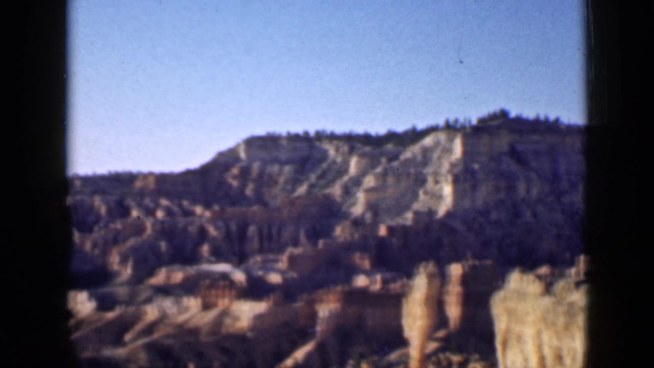 1939 Utah 8mm home-movie view of distant layered canyon walls, pale rock faces, and hoodoo spires framed by dark film edges.