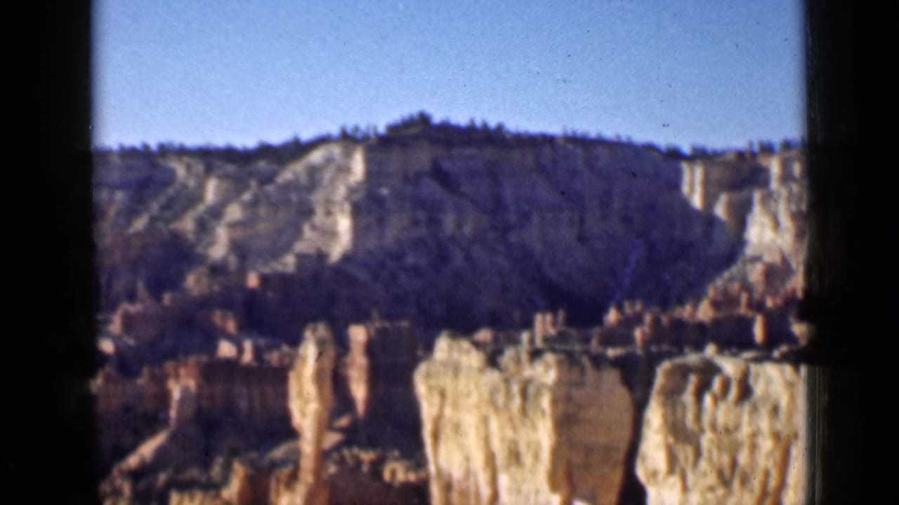 Canyon panorama with pale cliffs, hoodoos, and dark vertical film borders.