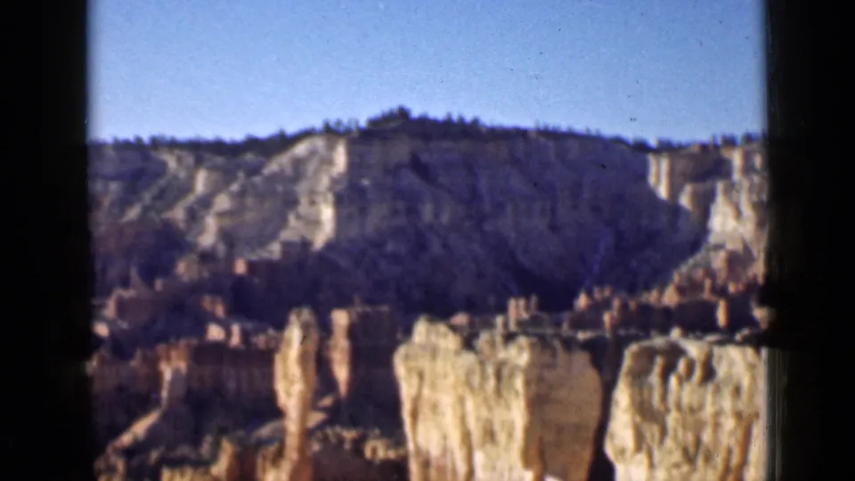 1939 Utah canyon pan showing eroded cliff bands, tall hoodoo forms, and a clear sky with visible 8mm frame borders.