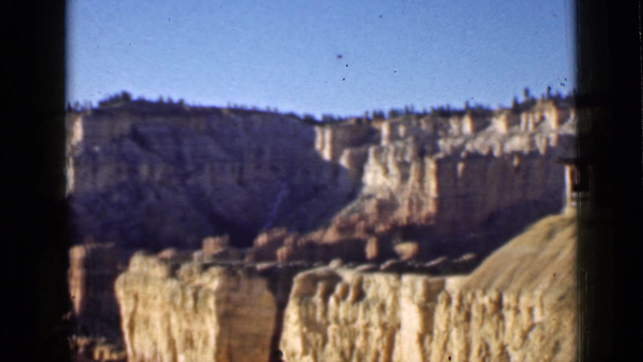 Utah 8mm home-movie frame from 1939 with a broad cliff face, foreground hoodoos, and warm faded color during the panorama.