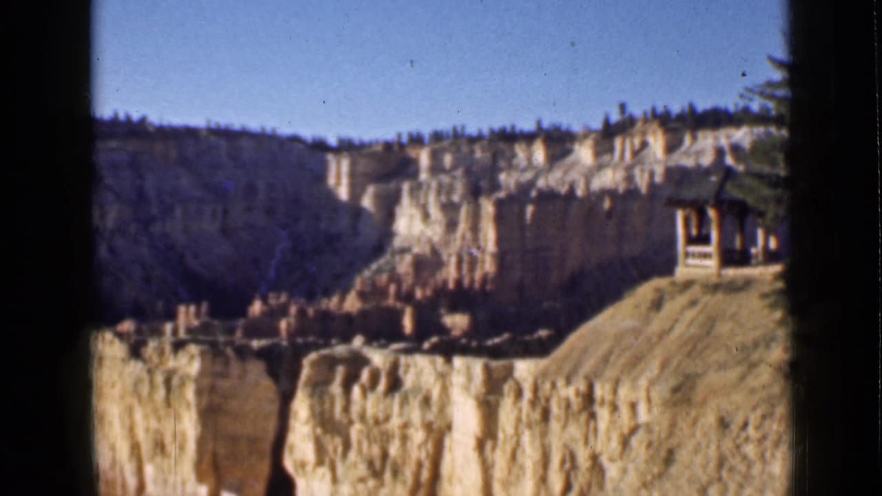 Final 1939 Utah canyon view with pale cliffs, hoodoo formations, and a small wooden observation shelter visible at the right edge.