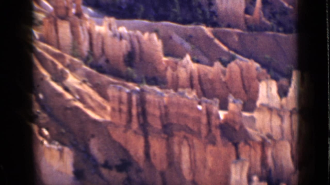 1939 Utah home-movie frame showing layered orange cliffs and pale hoodoo formations in a dry canyon landscape.