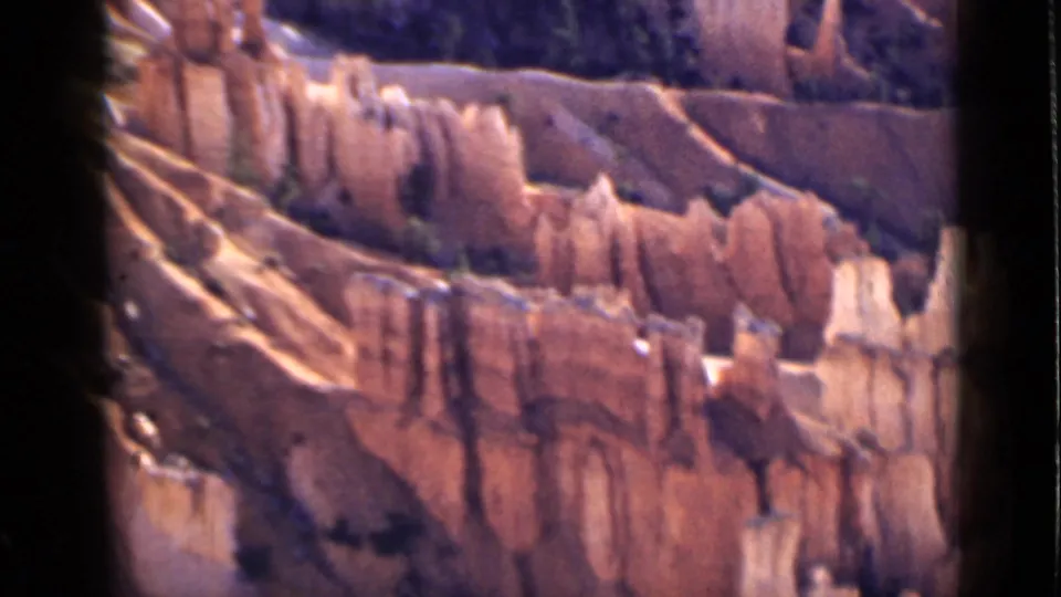 1939 Utah home-movie frame showing layered orange cliffs and pale hoodoo formations in a dry canyon landscape.