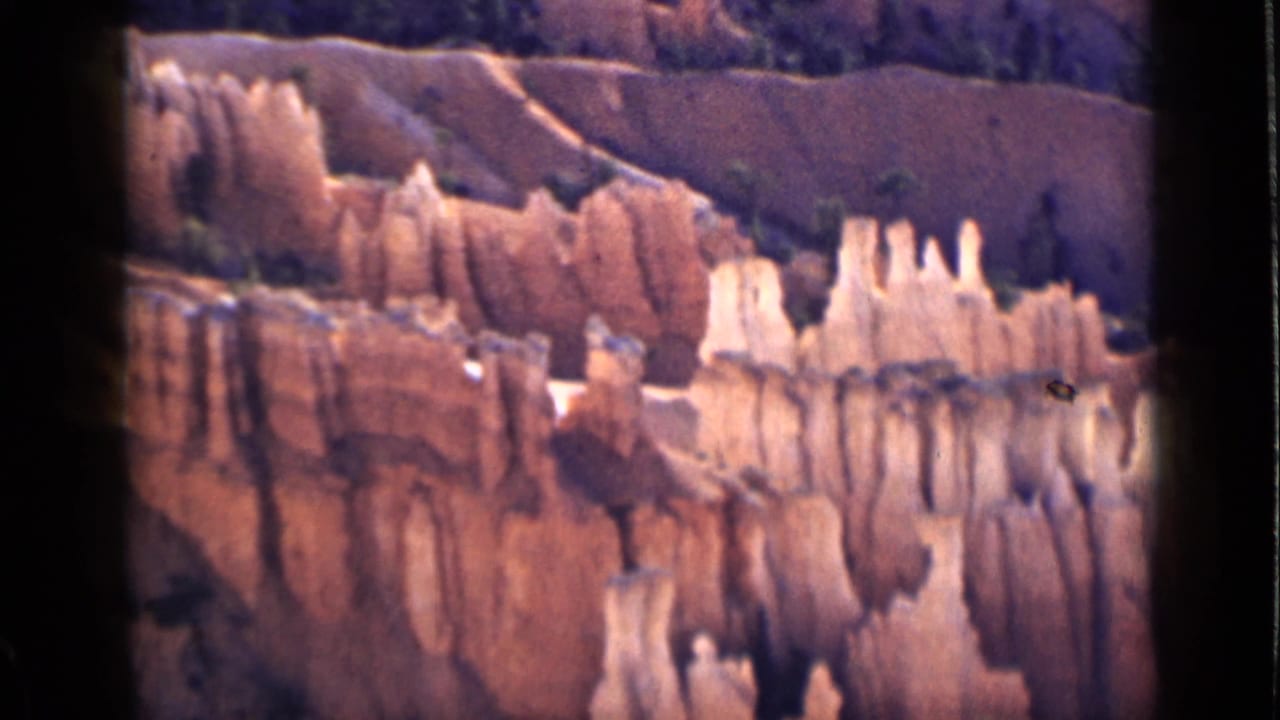 Eroded canyon wall with pale rock spires and reddish bands seen through 8mm frame edges.