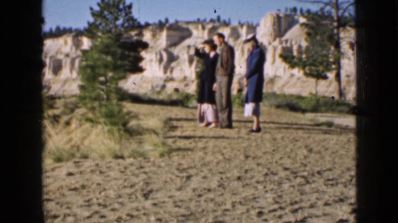 Three adult visitors pause together in a Utah scenic overlook area, with one person raising a hand toward the view.