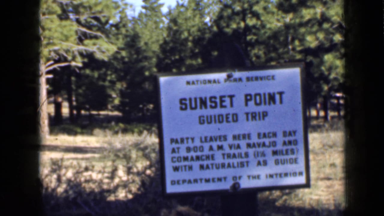 1939 Utah archival frame showing the Sunset Point Guided Trip sign at the edge of a wooded area.