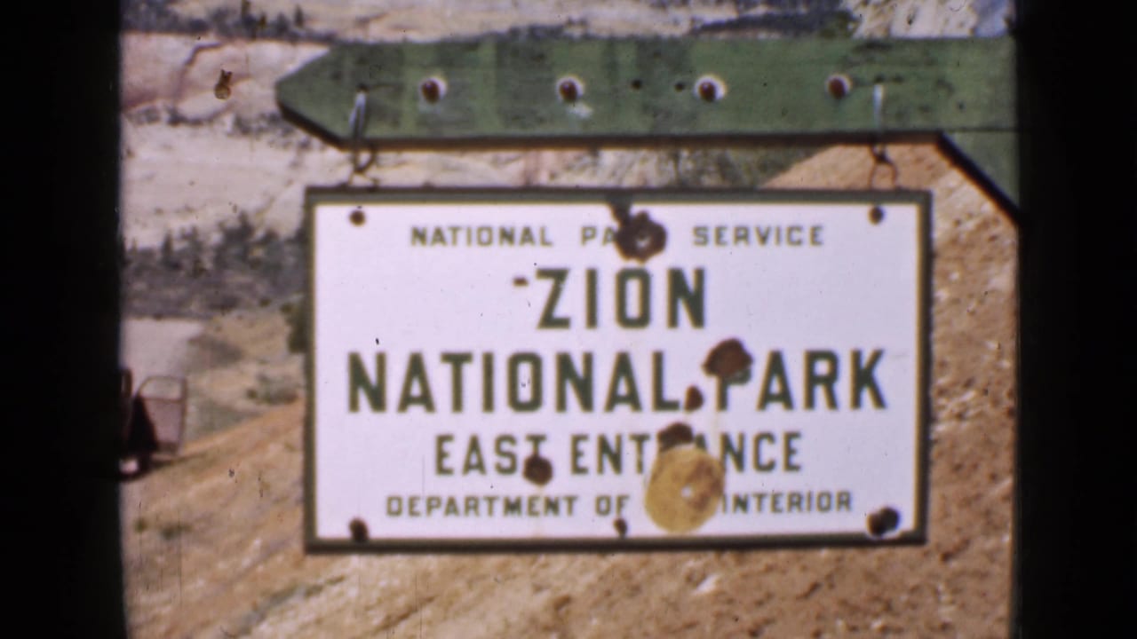 Zion National Park East Entrance sign seen through an 8mm frame with rocky terrain behind it.