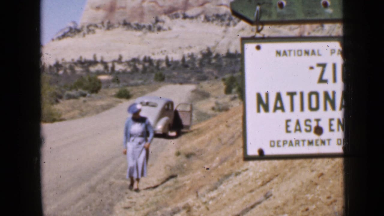 Woman on a dirt road near a parked car and Zion National Park East Entrance sign.