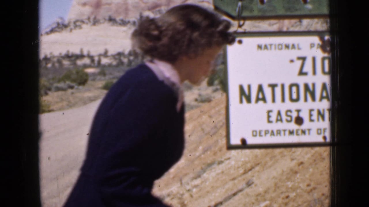 Woman passes close to the camera beside the Zion National Park East Entrance sign.