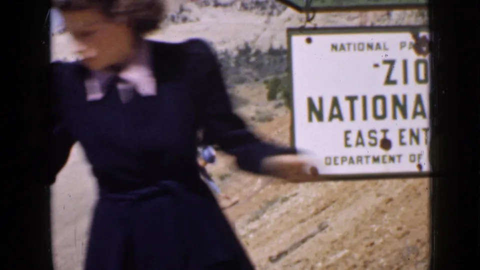 The 1939 home-movie frame shows the woman very close to camera, partially obscuring the Zion National Park East Entrance sign.