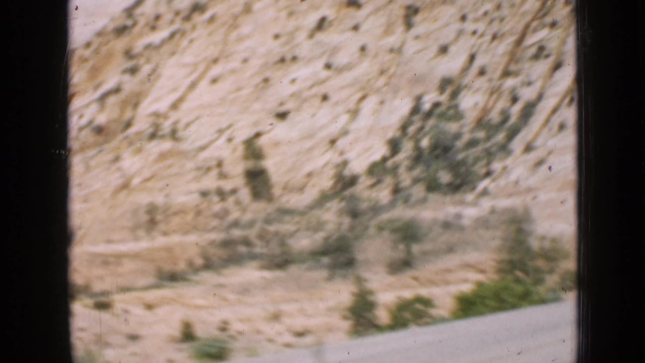A moving 8mm passenger view of arid Utah rock formations, low shrubs, and a roadway edge, with blur from the car's motion.