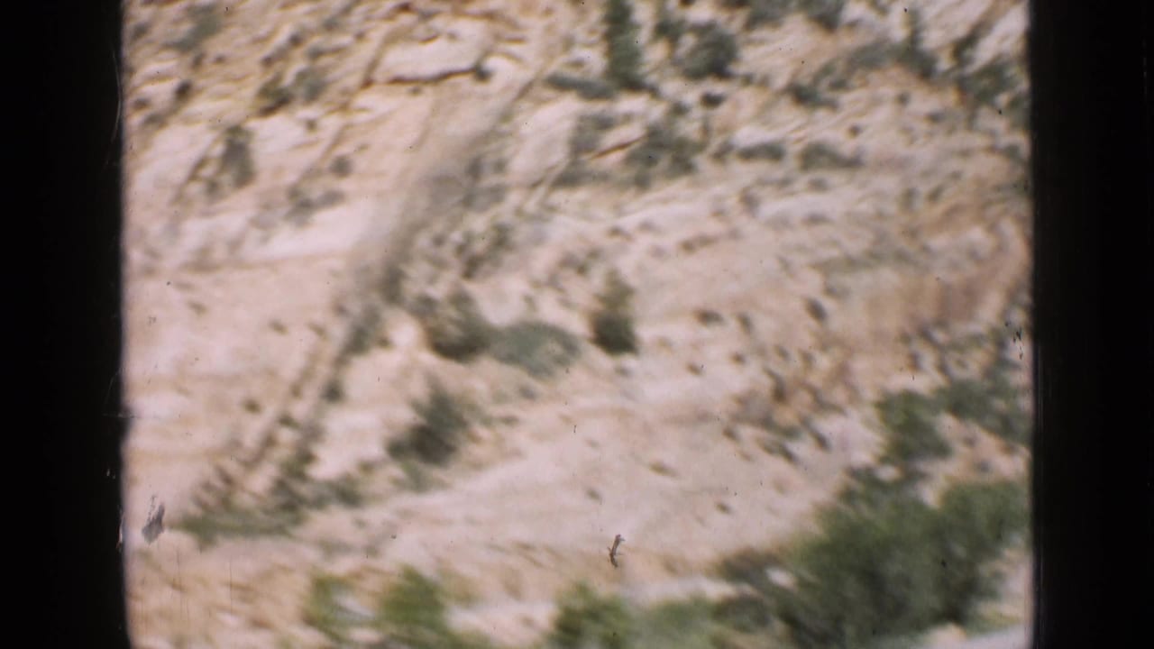 Utah canyon roadside filmed from a moving vehicle, with pale rock layers, scattered shrubs, and heavy motion blur in the 8mm frame.