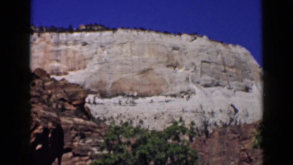 1939 Utah 8mm frame showing a sunlit pale rock formation above reddish rock and green shrubs under clear blue sky.