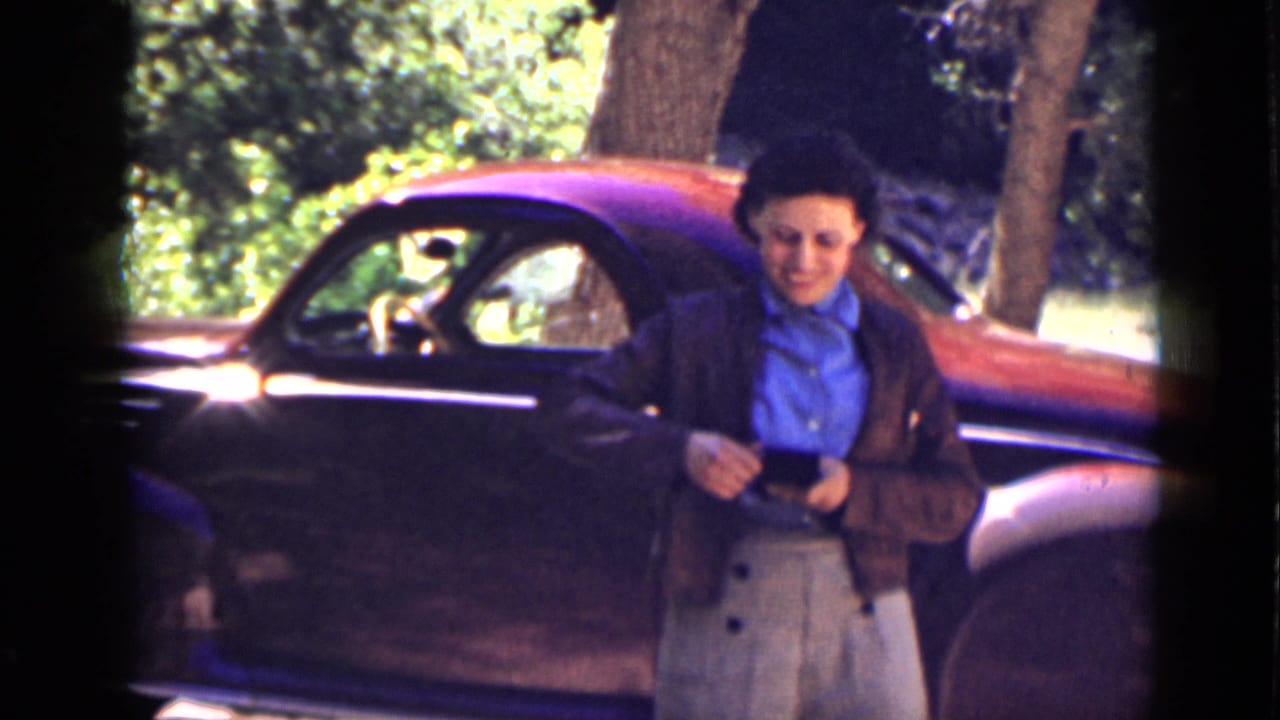A woman faces the camera beside a dark-and-red classic car, with trees and canyon shade visible in the Utah travel scene.