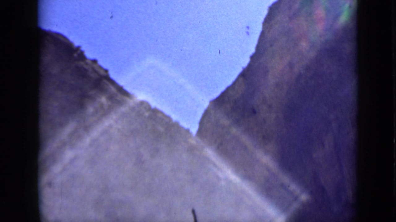 A handheld 8mm view appears to look up through rocky Utah canyon walls toward a clear blue sky, with flare across the frame.