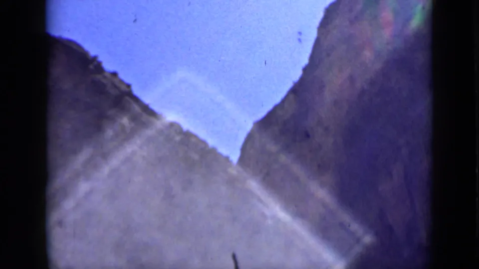A handheld 8mm view appears to look up through rocky Utah canyon walls toward a clear blue sky, with flare across the frame.