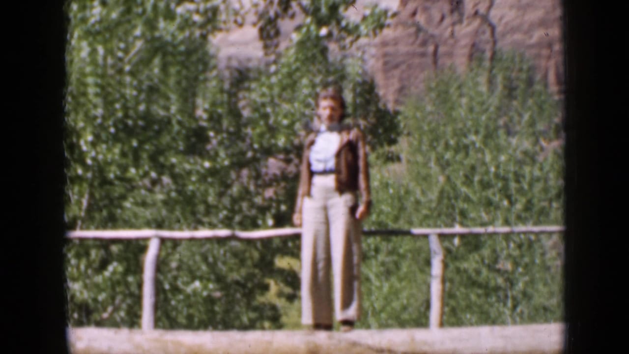 Woman standing on a rustic log bridge with trees and rock formations behind her.