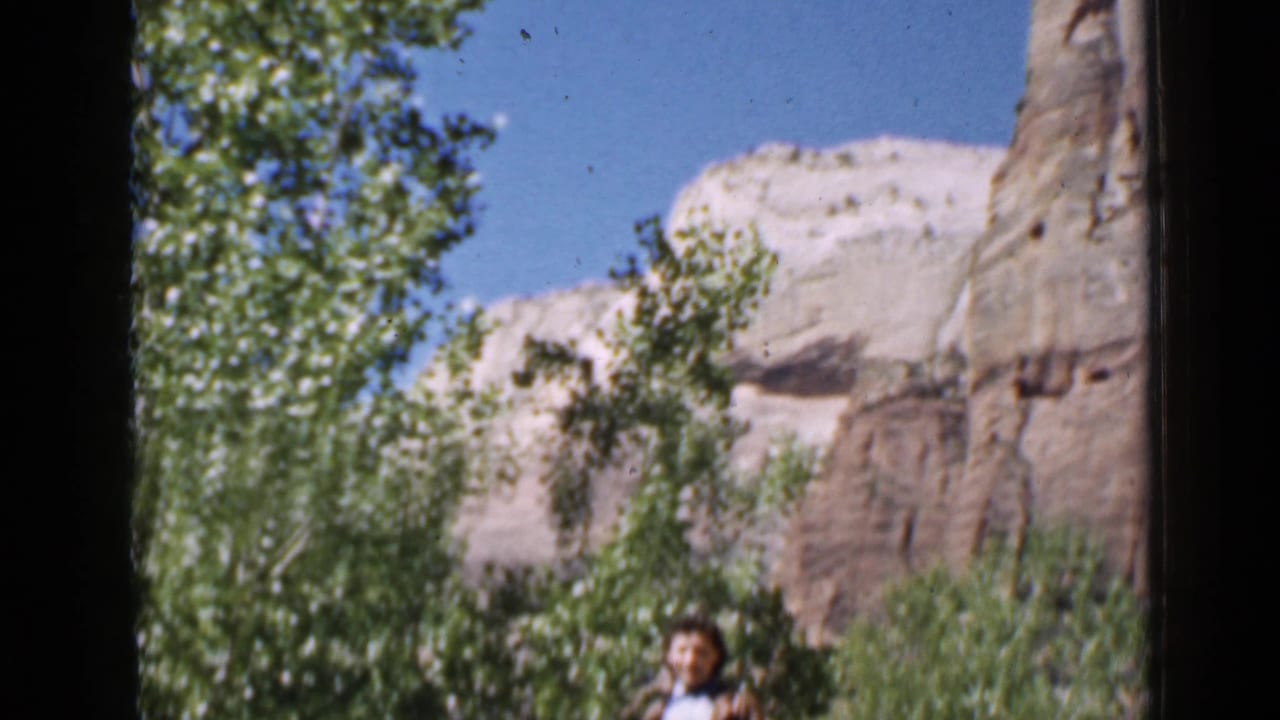 A woman appears low in frame beneath trees, with Utah rock formations and bright blue sky visible in the 1939 home-movie shot.