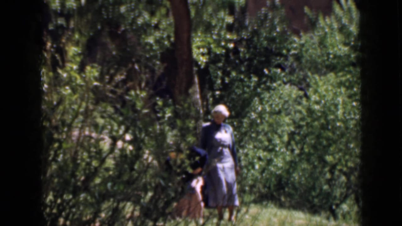Two women are visible among green trees and grass in a Utah outdoor setting, one nearer the camera and another partly obscured.