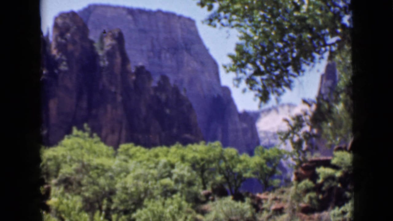 1939 Utah travel footage frame showing dark canyon formations, green vegetation, and shaded tree framing.