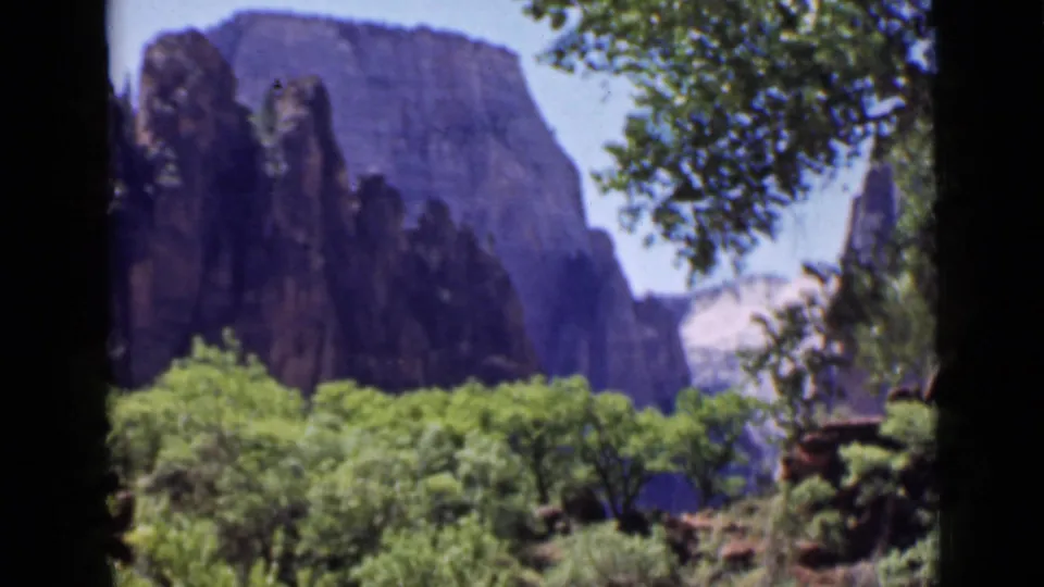 1939 Utah travel footage frame showing dark canyon formations, green vegetation, and shaded tree framing.