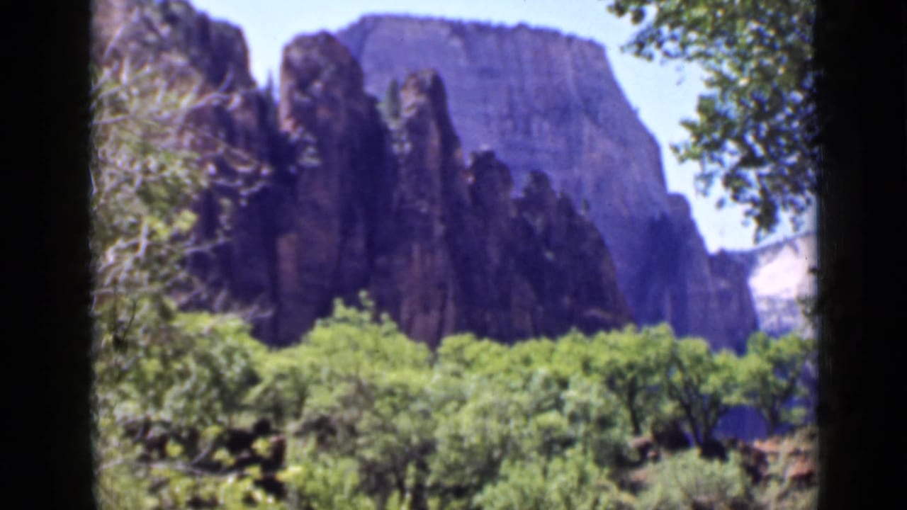 1939 Utah 8mm frame showing tall rock cliffs beyond green trees and shrubs, with soft focus and dark film edges.