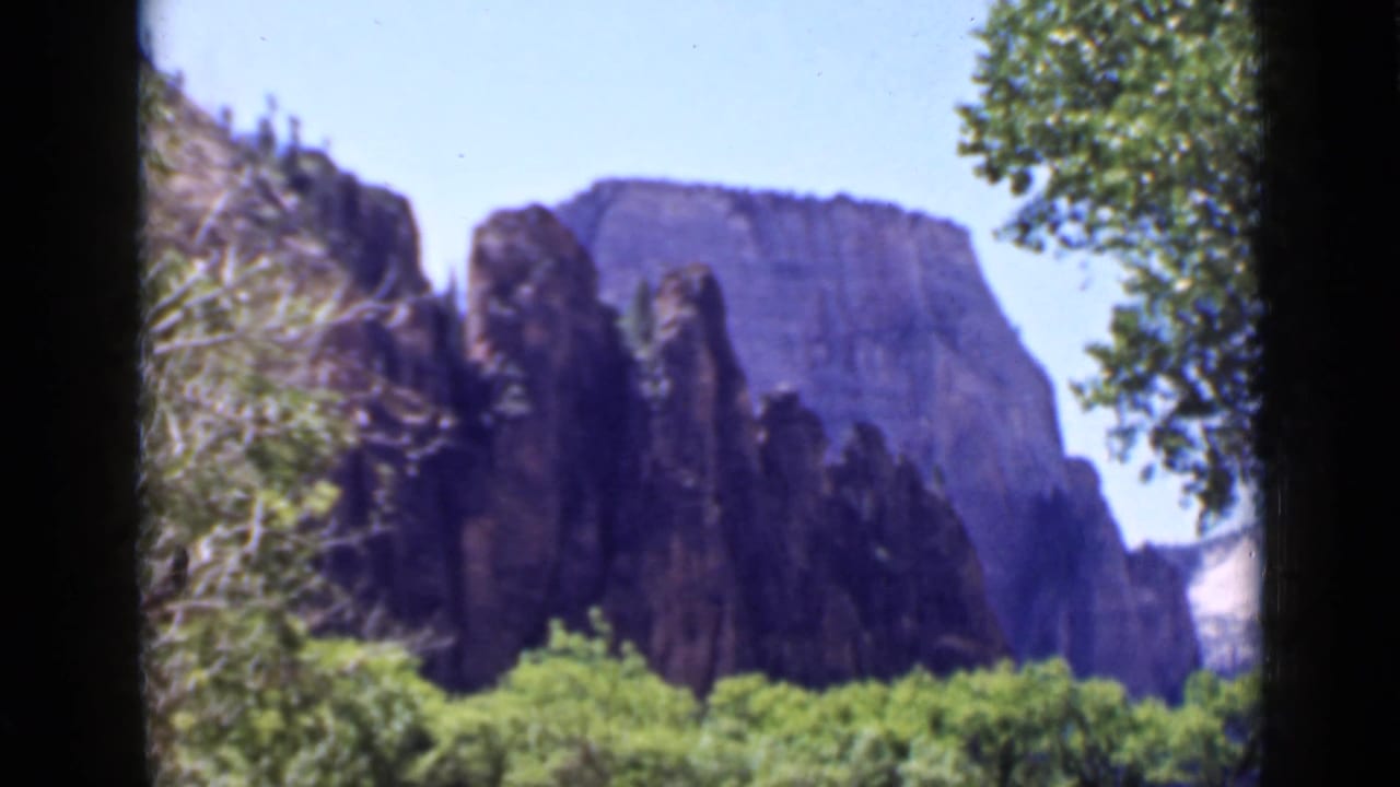 1939 Utah 8mm view of rugged cliffs behind leafy trees, with branches framing the scene and soft color-film texture.