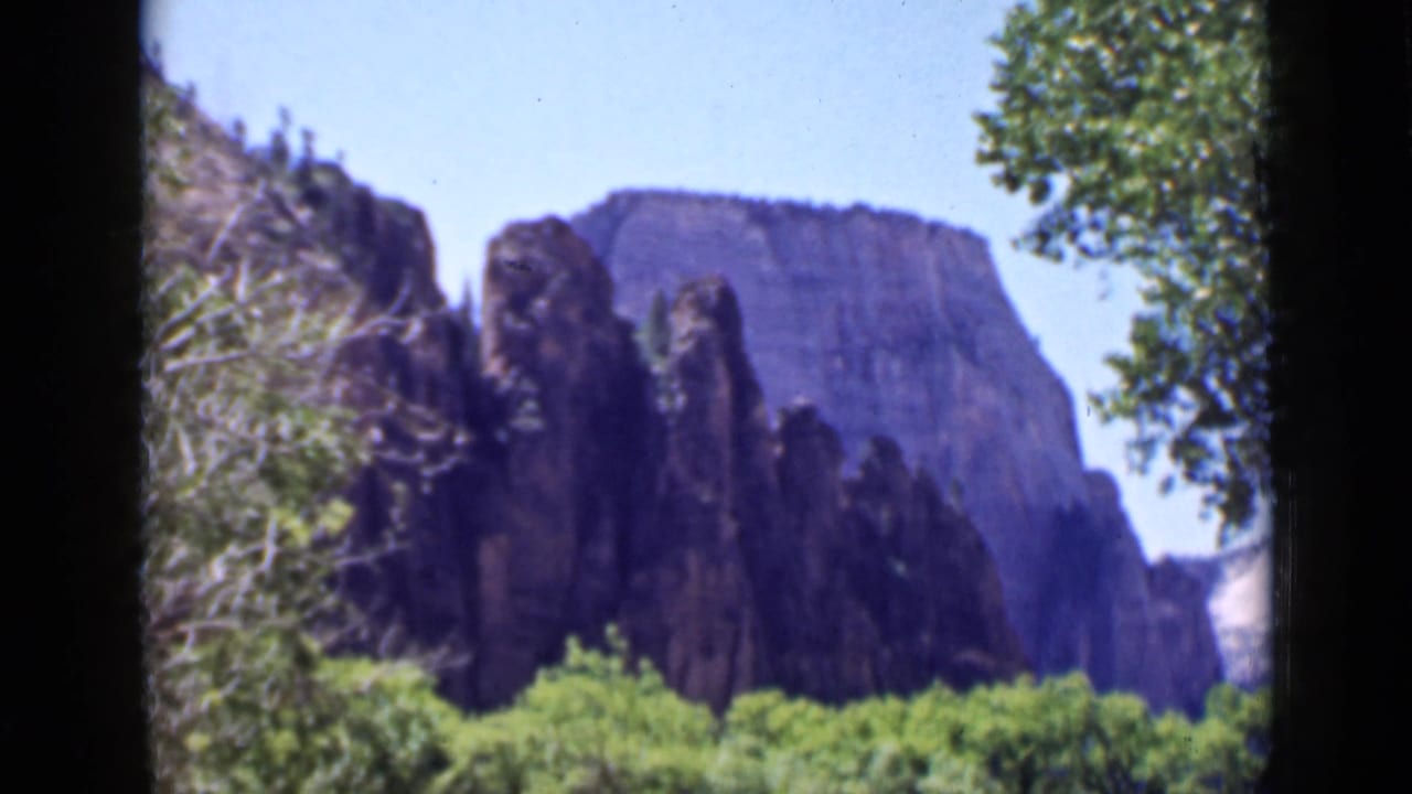 1939 Utah 8mm frame of cliff faces and narrow rock forms beyond trees and brush, with saturated greens and soft focus.