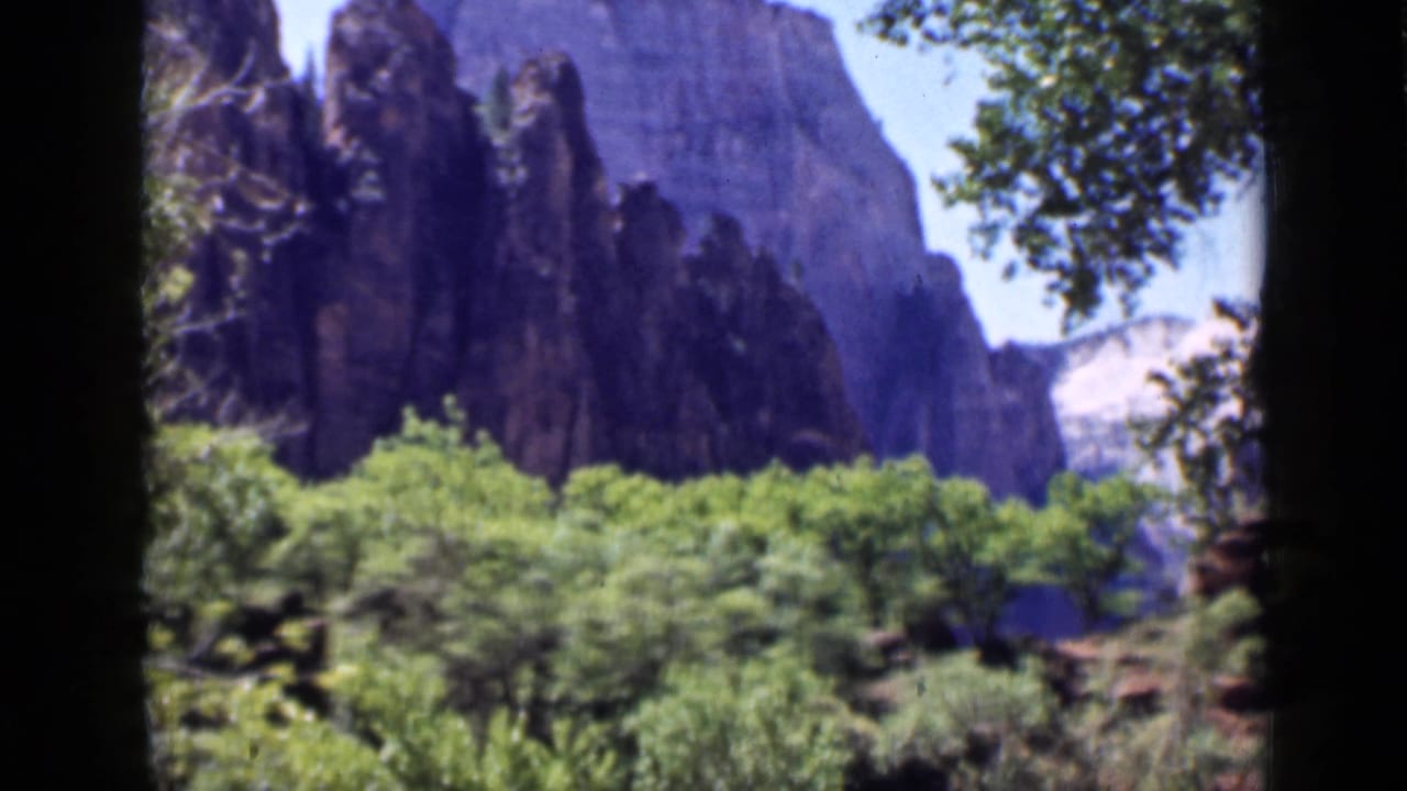 1939 Utah 8mm frame showing tall rock formations above green trees, with branches and dark film borders framing the view.