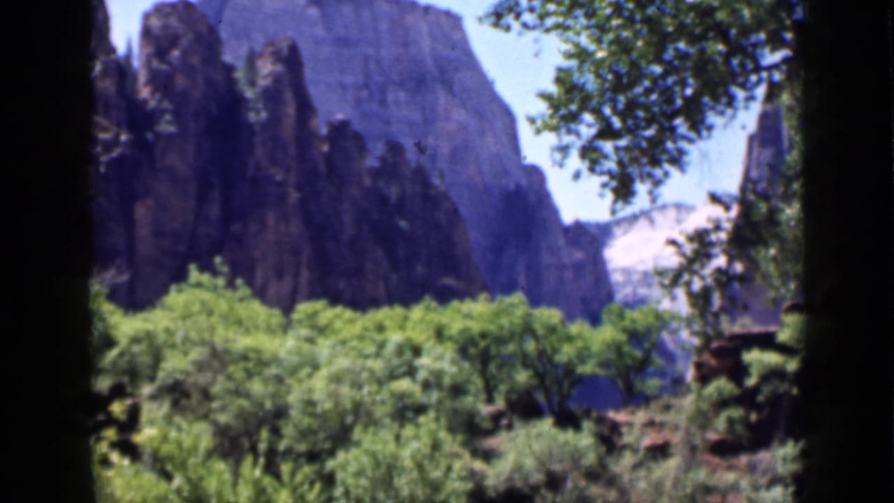 1939 Utah 8mm frame with towering rock formations behind a band of green trees and brush.