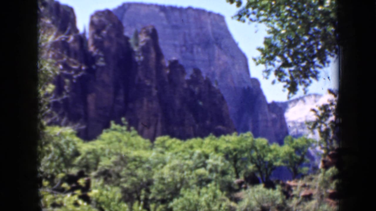 1939 Utah landscape frame showing sandstone cliffs, dense trees, and bright sky in soft color 8mm footage.