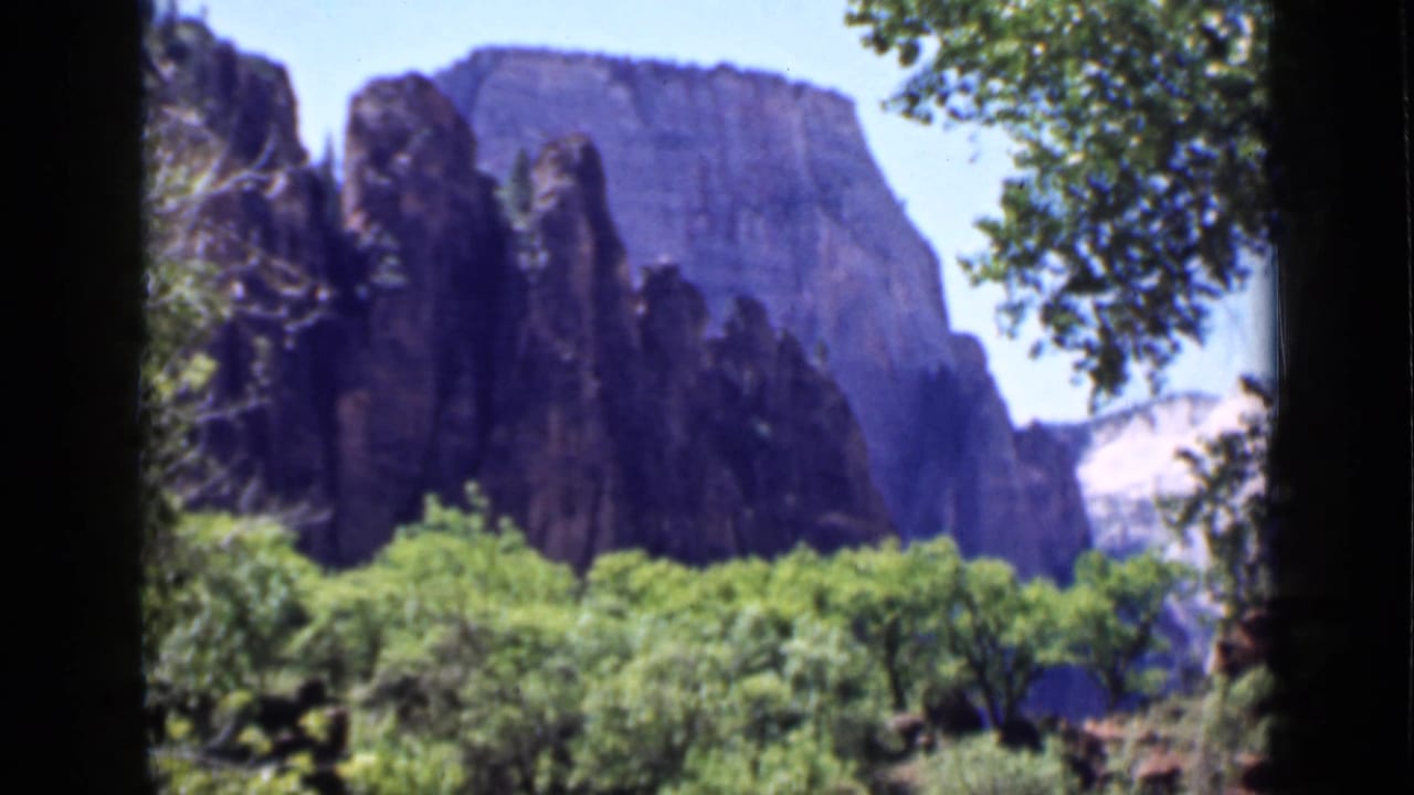 1939 Utah 8mm view of jagged mountain cliffs rising behind green trees under a pale sky.