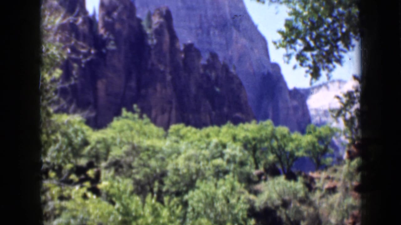 Rock wall and green trees framed by dark vertical film borders.